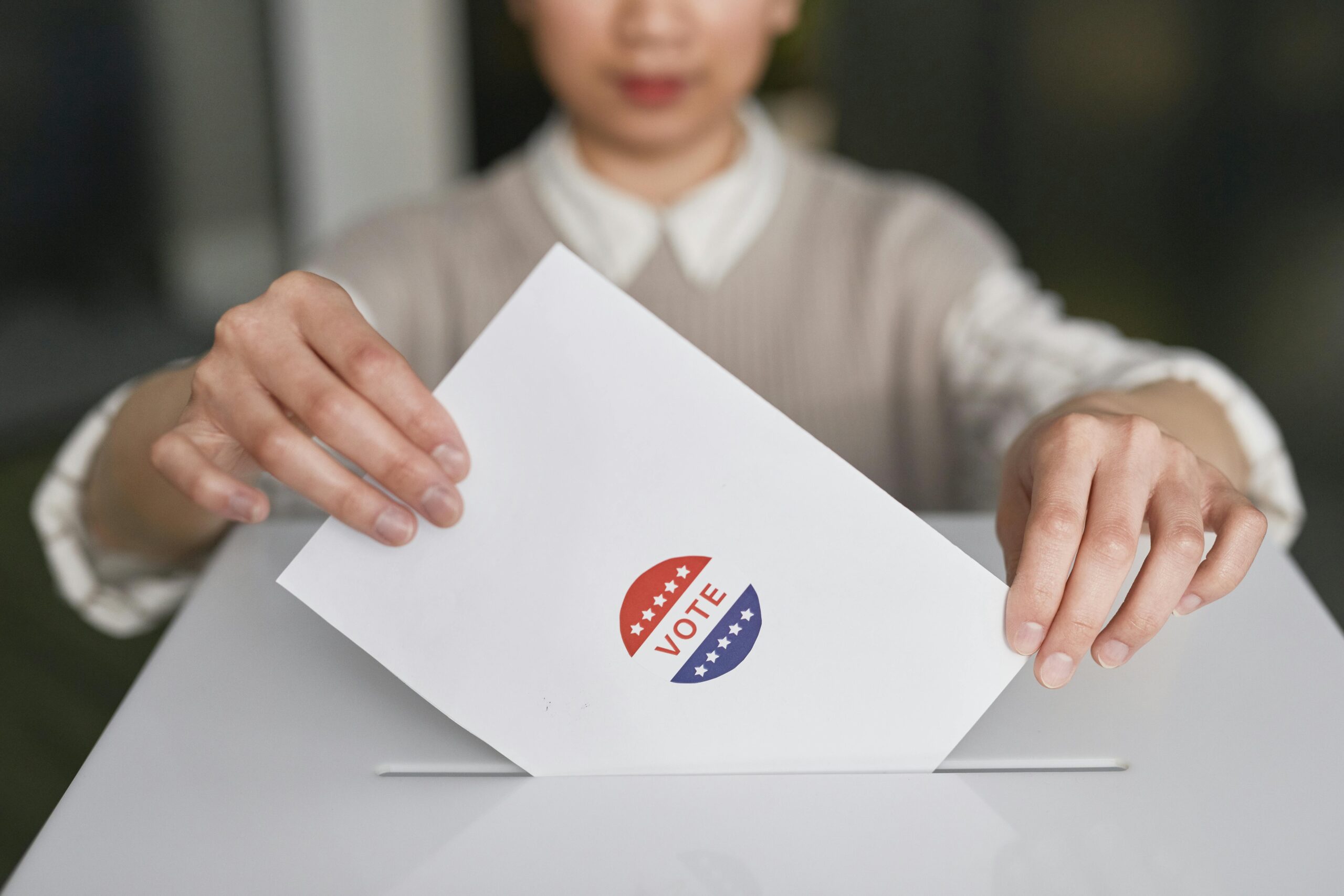 Woman putting ballot with 'VOTE' sticker into the ballot box