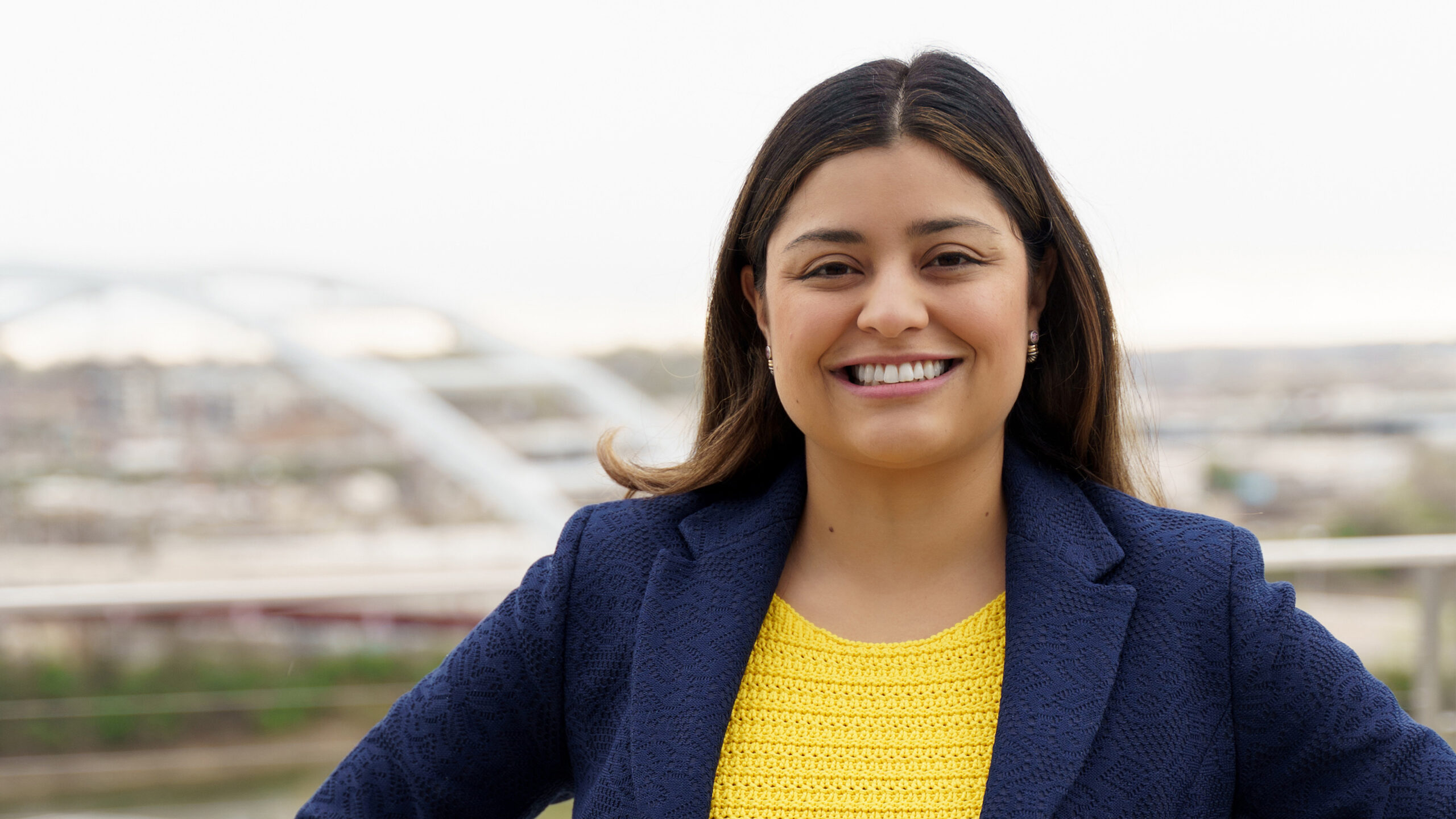 Headshot of Laura Zapata, the CEO of Clearloop - standing in front of Washington DC background in yellow shirt and blue blazer.